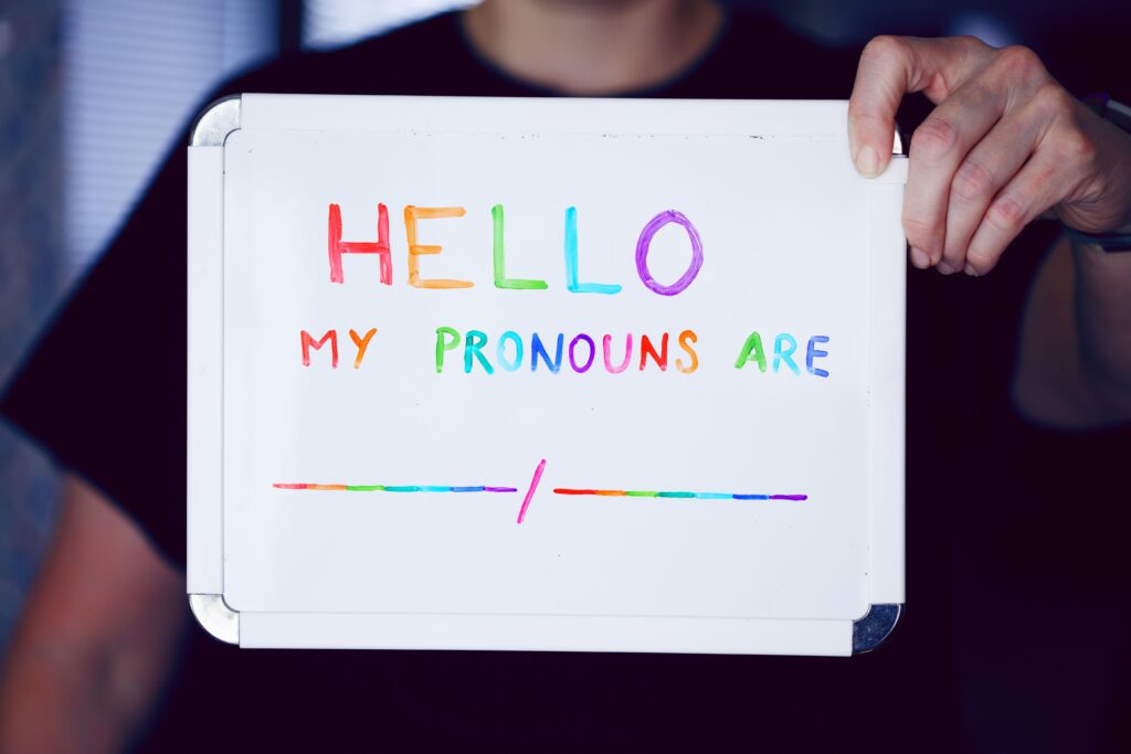 queer κρατάει λευκή πινακίδα που αναγράφει τα pronouns που χρησιμοποιεί
