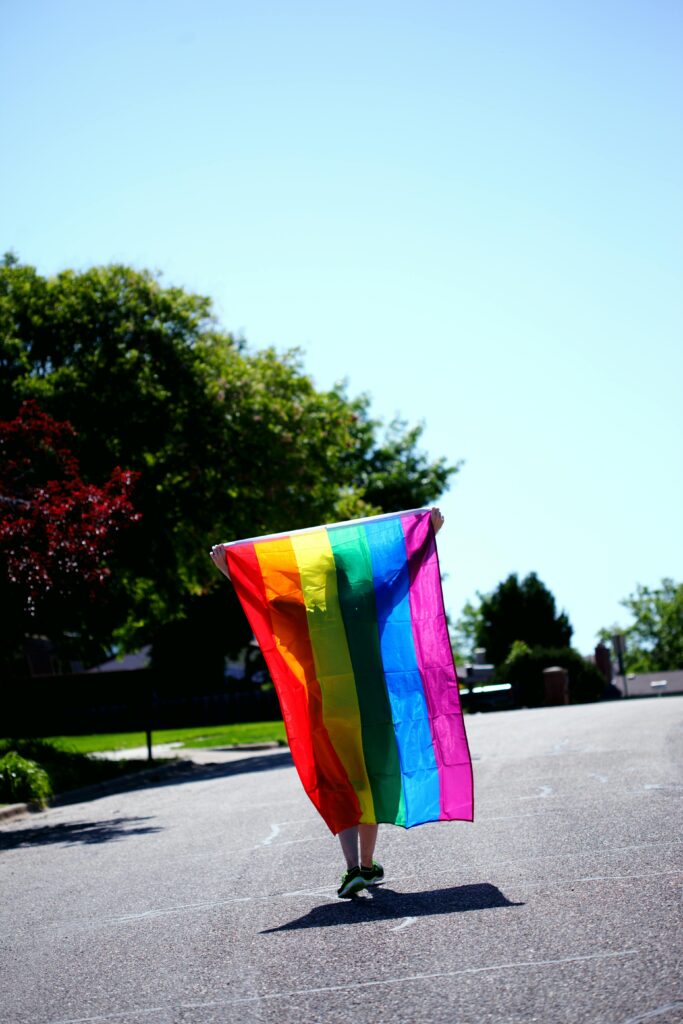 κουίρ άτομο γυρισμένο πλάτη κρατάει την LGBTQ+ σημαία